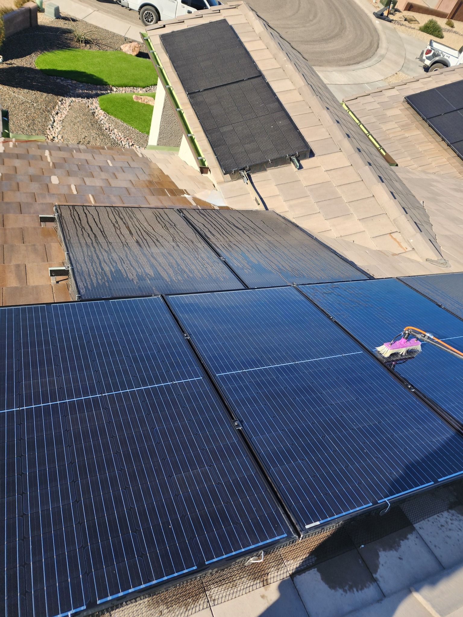 Technician cleaning rooftop solar panels with a water-fed pole