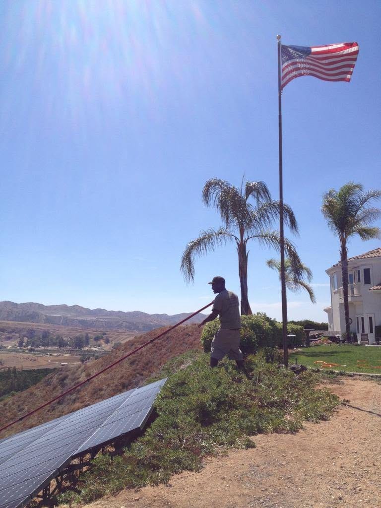 Technician cleaning ground-mounted solar panels near a hillside
home